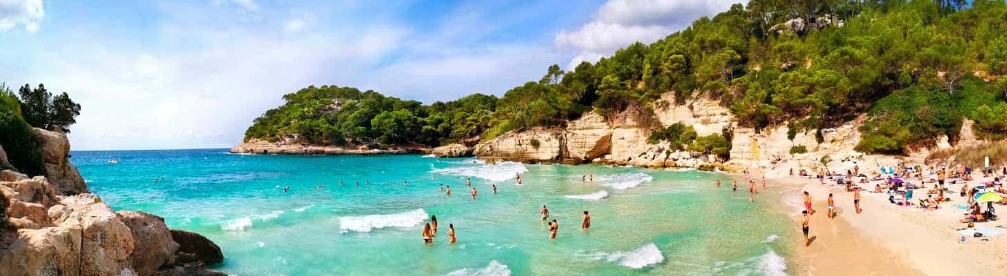 People swimming in the blue sea at Cala Mitjana resort in Menorca